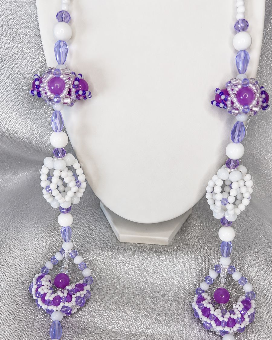 Collar artesanal de cuentas blancas y moradas con adornos tejidos, sobre busto